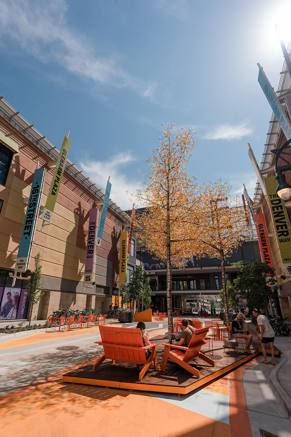 Vibrant outdoor plaza with orange seating, trees, and colorful banners.